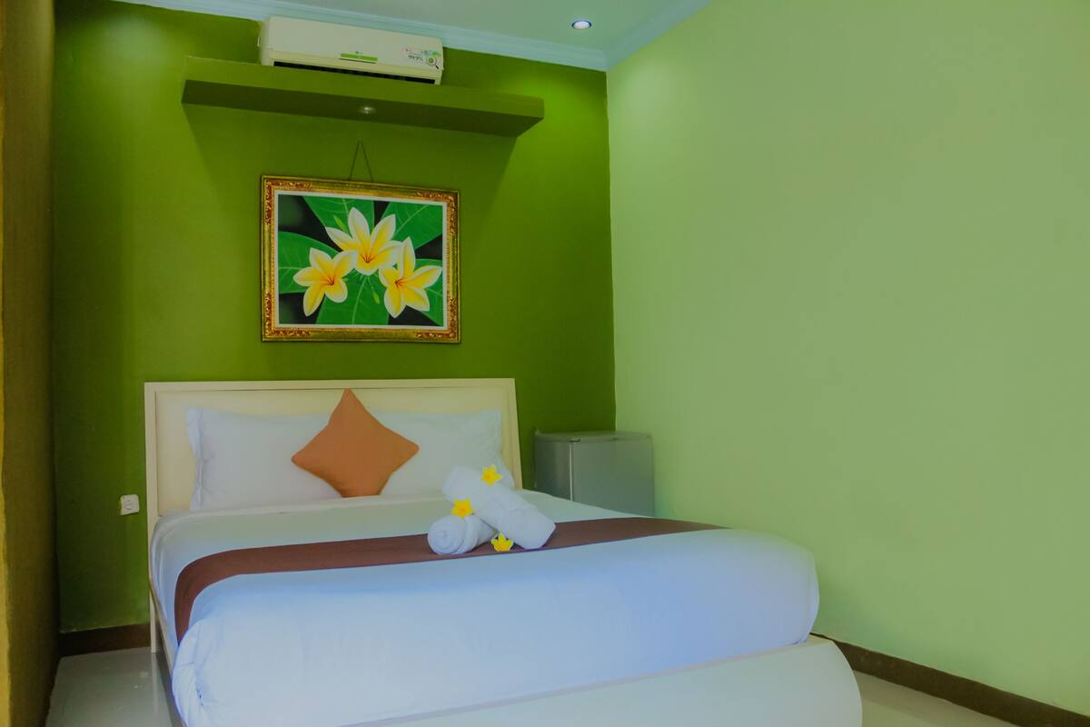 Uma cama bem arrumada com lençóis brancos e detalhes em marrom, um quadro com flores na parede e um pequeno aparelho de ar condicionado sobre a cama.