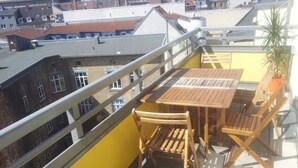 Un balcón con una mesa y sillas de madera, una planta en maceta y vistas a edificios.