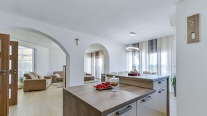 Una cucina moderna con isola centrale, zona pranzo con tavolo e sedie, e soggiorno con divano e tavolino.