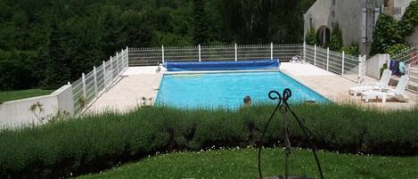 A rectangular swimming pool with a white fence, surrounded by a grassy area and a stone building.