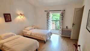 Ein Schlafzimmer mit zwei Betten, einem Heizkörper, einem Fenster mit Vorhängen und einer Tür.