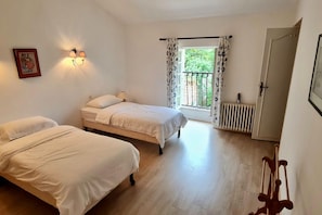 Quarto com duas camas, um radiador, uma janela com cortinas e uma porta.