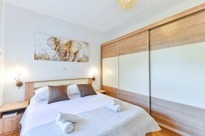Een net opgemaakt bed met een wit-bruine sprei, een houten hoofdbord en een groot kunstwerk van een olifant aan de muur.
