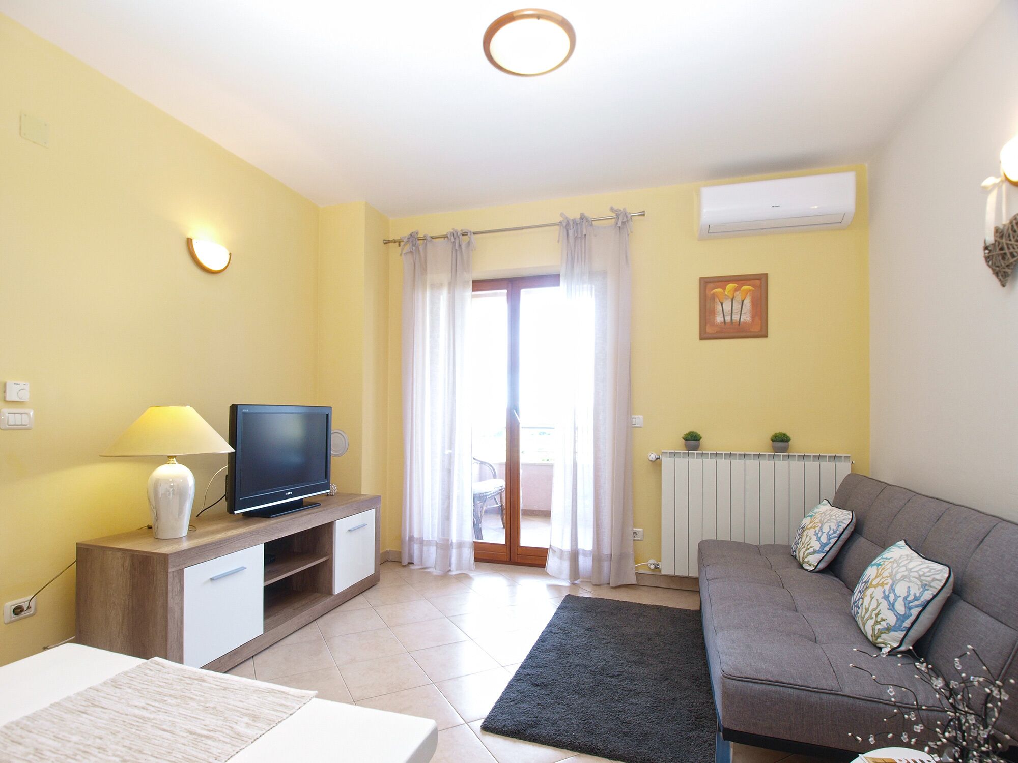 Una sala de estar con televisión, sofá y ventana con cortinas.
