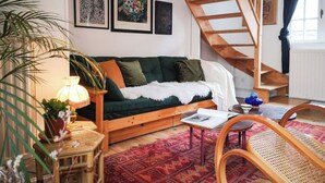 Una sala de estar acogedora con una escalera de madera, un sofá verde, una mesita pequeña y una silla de ratán.
