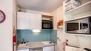 Et kompakt køkken med opvaskemaskine, mikroovn, toaster og lille ovn.