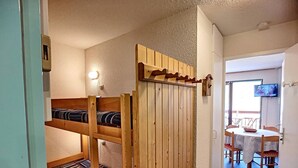 Et værelse med køjesenge, et spiseområde med et bord og stole, samt et fjernsyn ophængt på væggen.