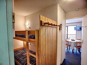 Ett rum med våningssängar, en matplats med bord och stolar samt en tv som är monterad på väggen.
