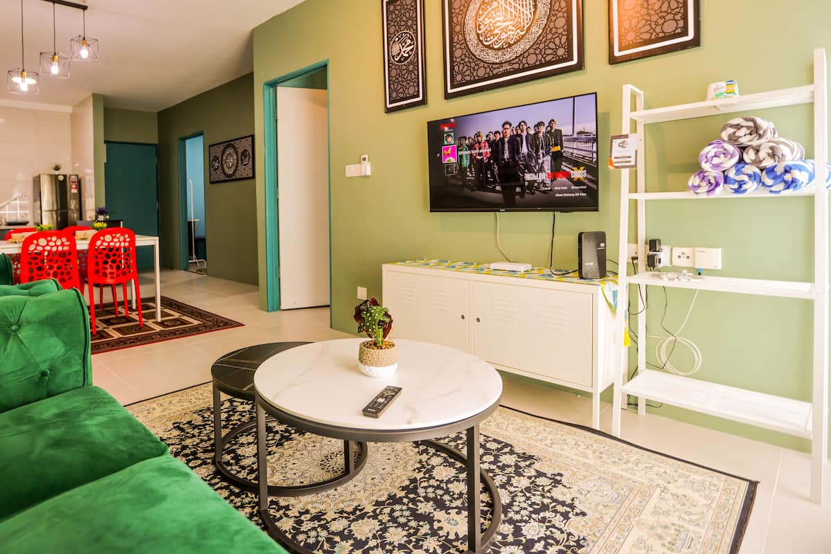 Una sala de estar con un sofá verde, una mesa de centro blanca y un televisor montado en la pared.