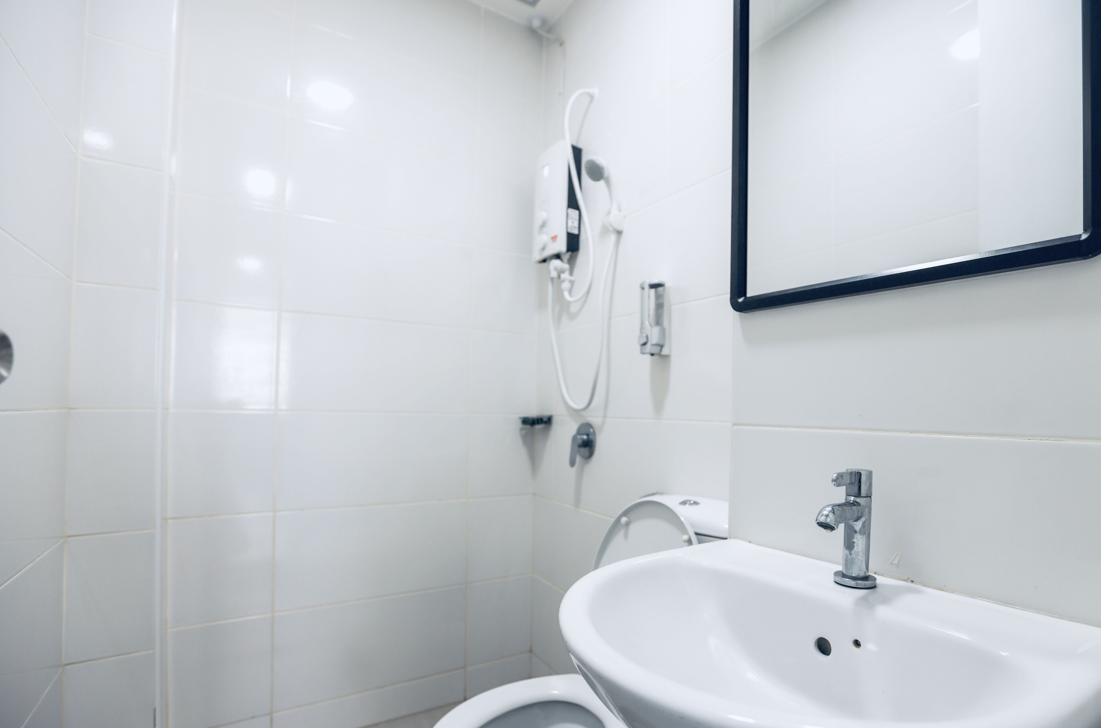 Un baño moderno con baldosas blancas, un lavabo, un espejo y una ducha.