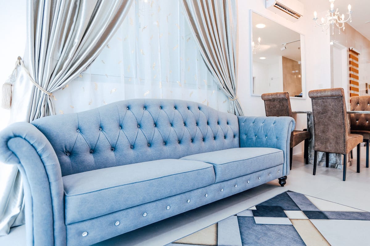 Una sala de estar moderna con un sofá azul, un comedor con sillas marrones y una cocina con armarios blancos.