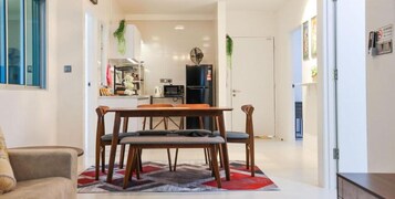 A modern living room with a wooden dining table and chairs, a sofa, and a kitchen in the background.