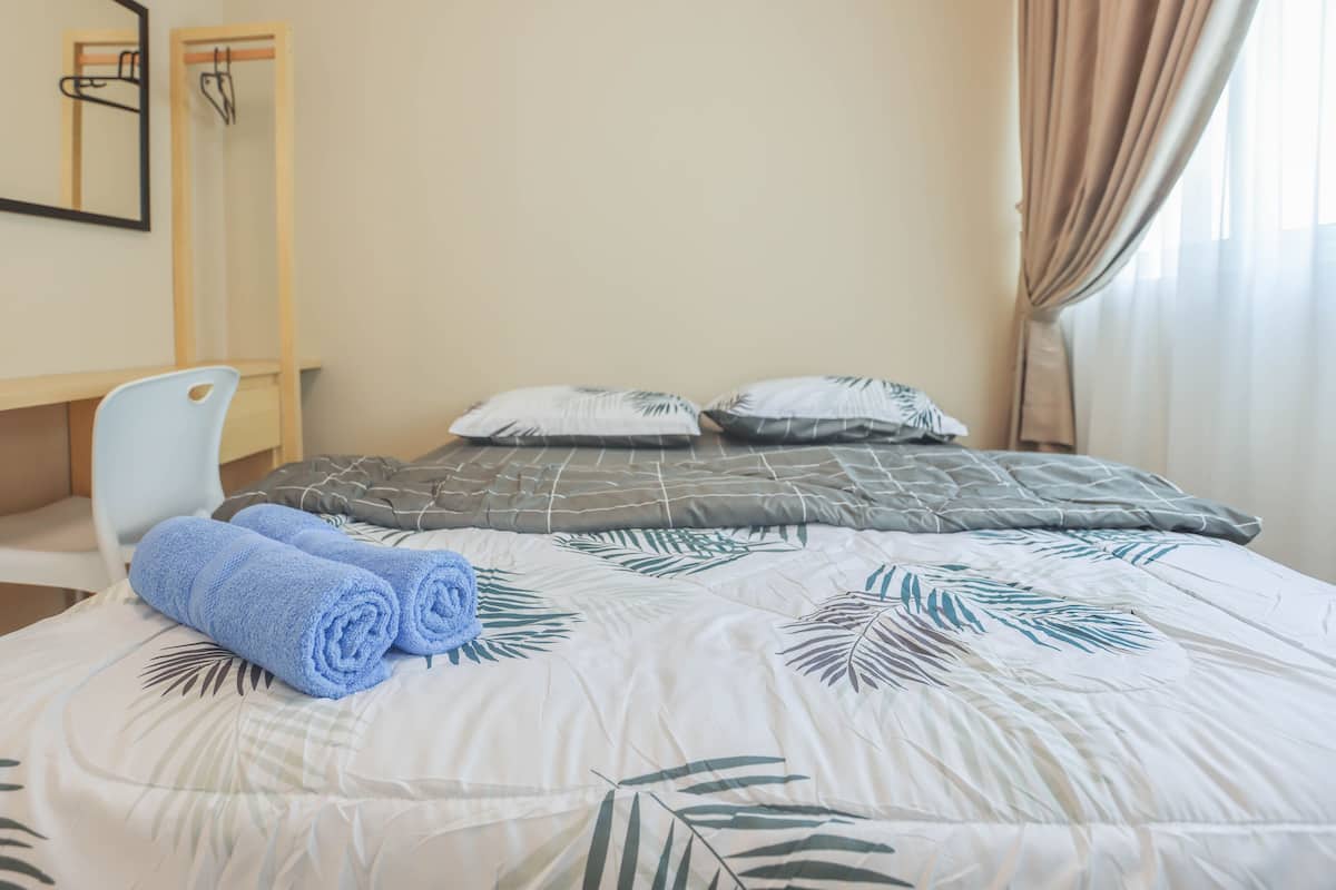 Una cama bien tendida con un edredón estampado con hojas, una silla y un escritorio con un espejo y objetos colgando.