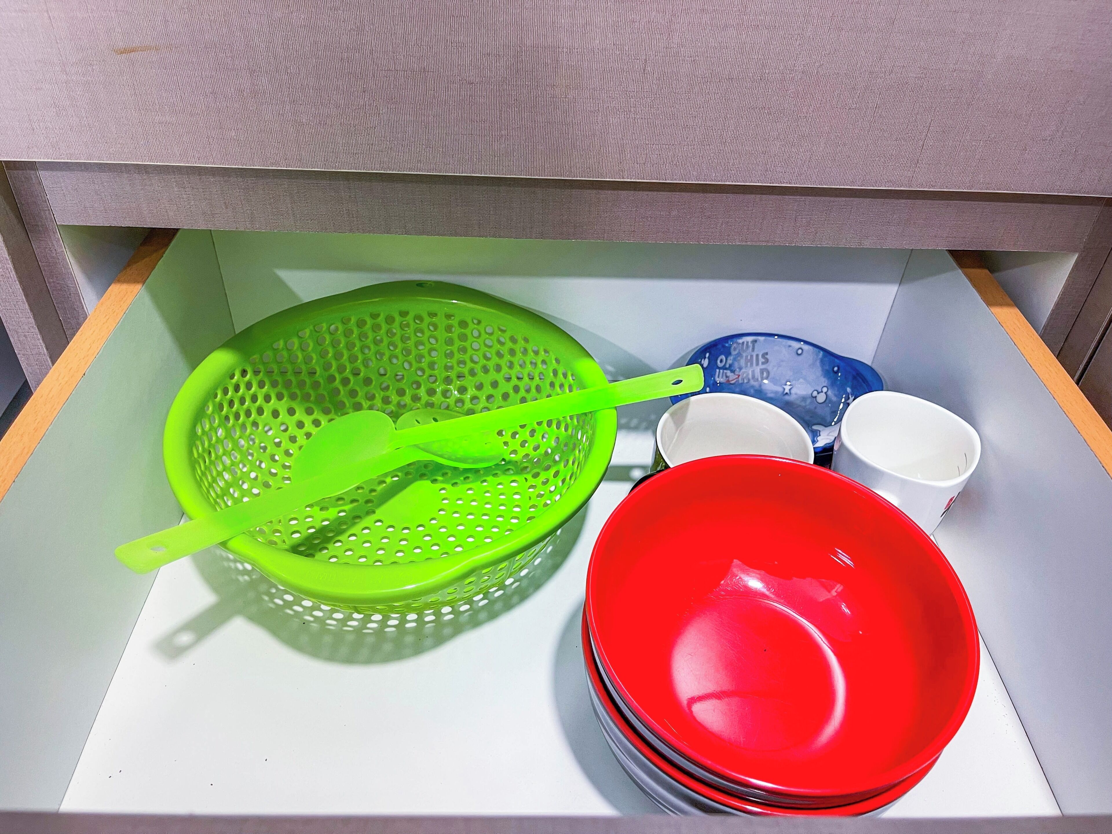 Un tiroir de cuisine contenant une passoire verte, un saladier rouge et une assiette bleue.
