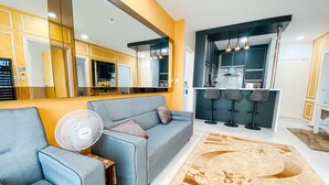 Een moderne woonkamer met een grijze bank, een staande ventilator en een kamerkleed met patroon.