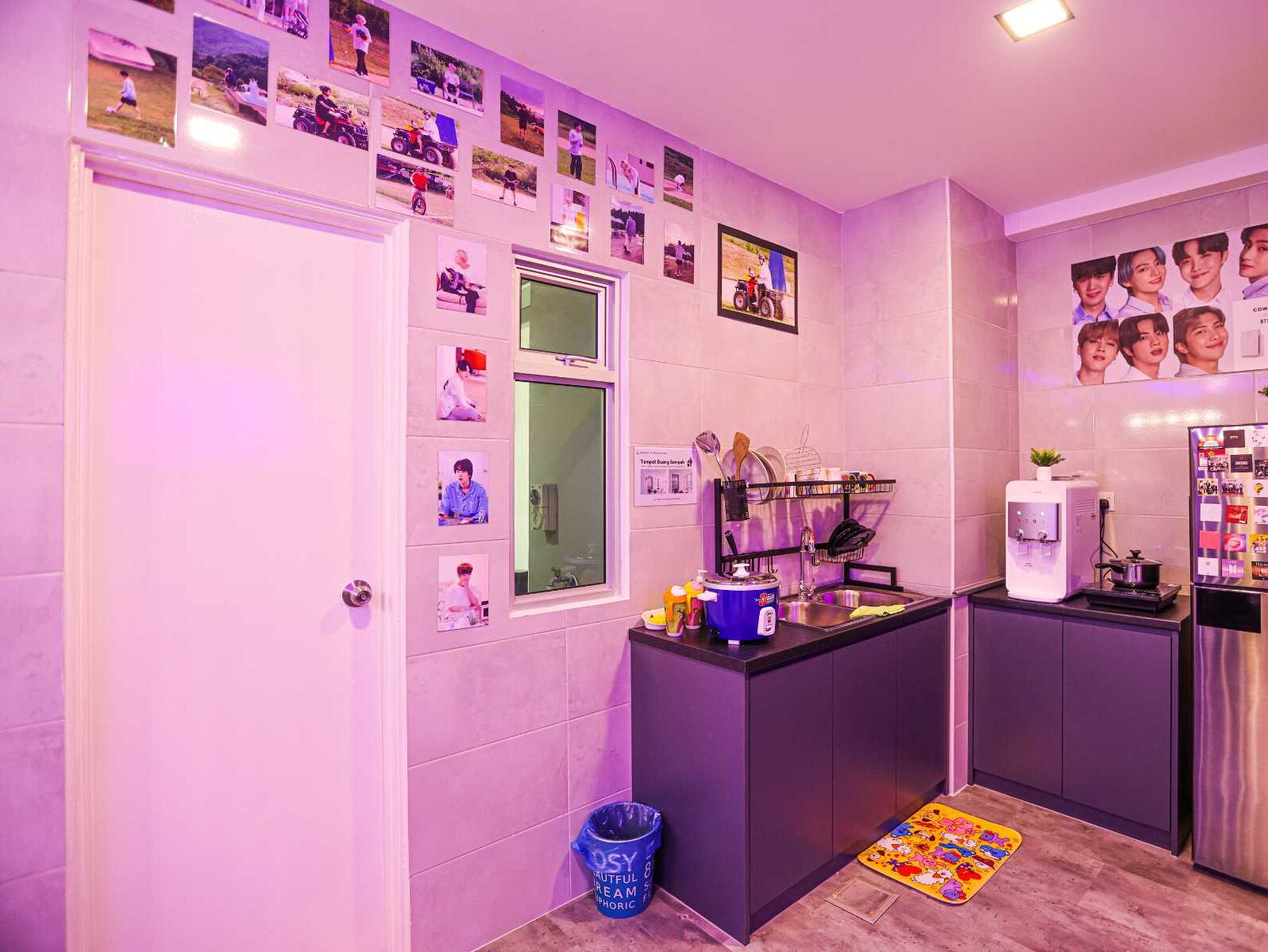 A compact kitchen with a sink, a coffee machine, and a refrigerator. There are photos on the wall and a small rug on the floor.