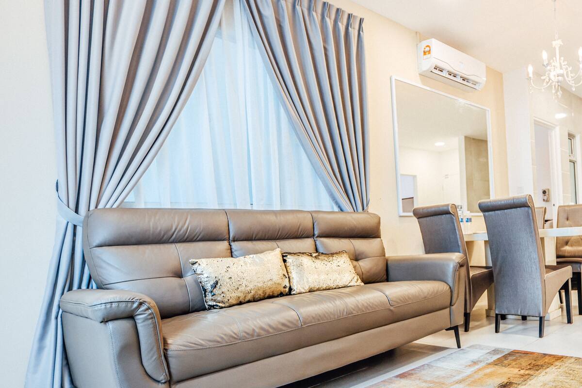 Una sala de estar moderna con un sofá de cuero, un comedor con mesa y sillas, y un gran ventanal con cortinas.