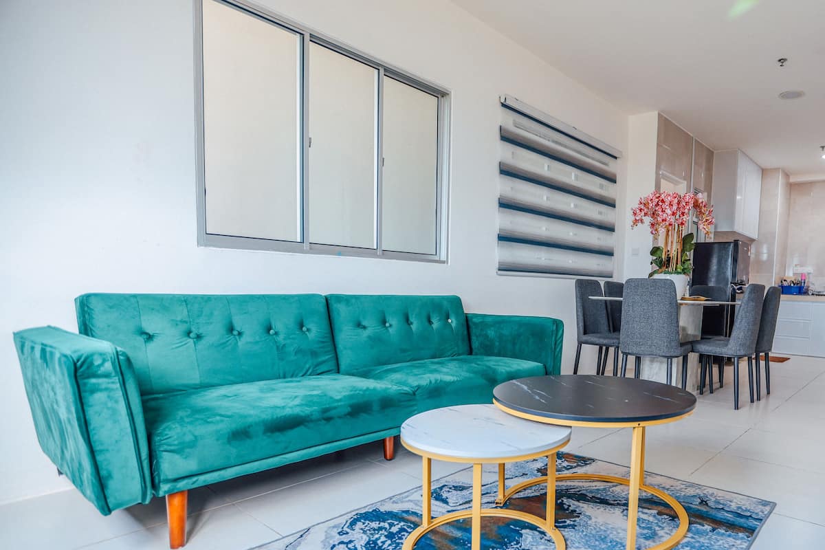 Un sofá azul verdoso, dos mesitas redondas y una cocina moderna al fondo.