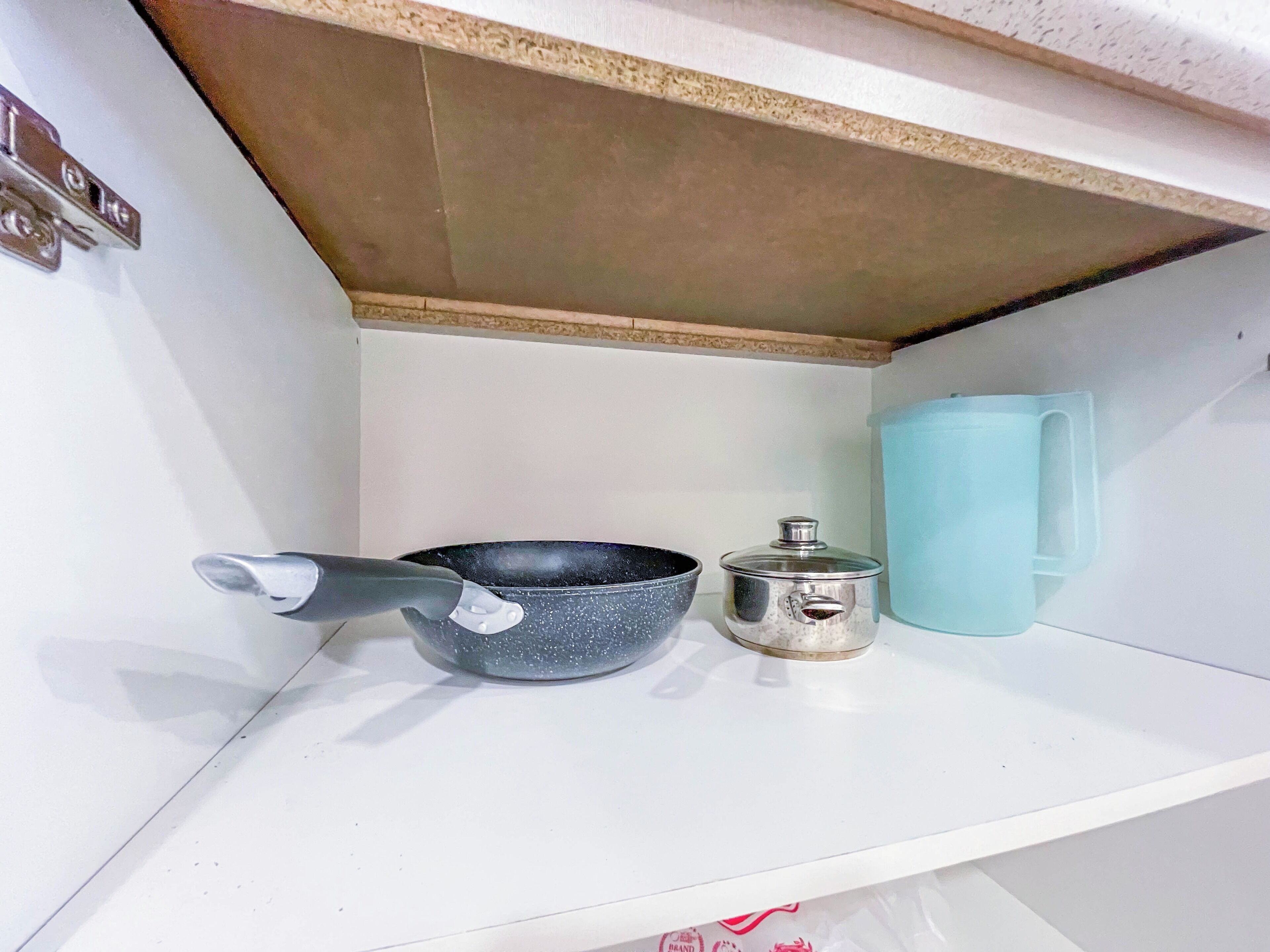 A kitchen shelf with a frying pan, a pot, and a blue mug.