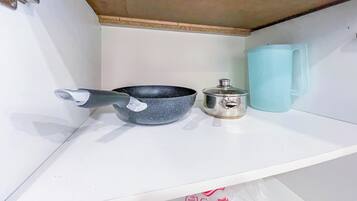 A kitchen shelf with a frying pan, a pot, and a blue mug.