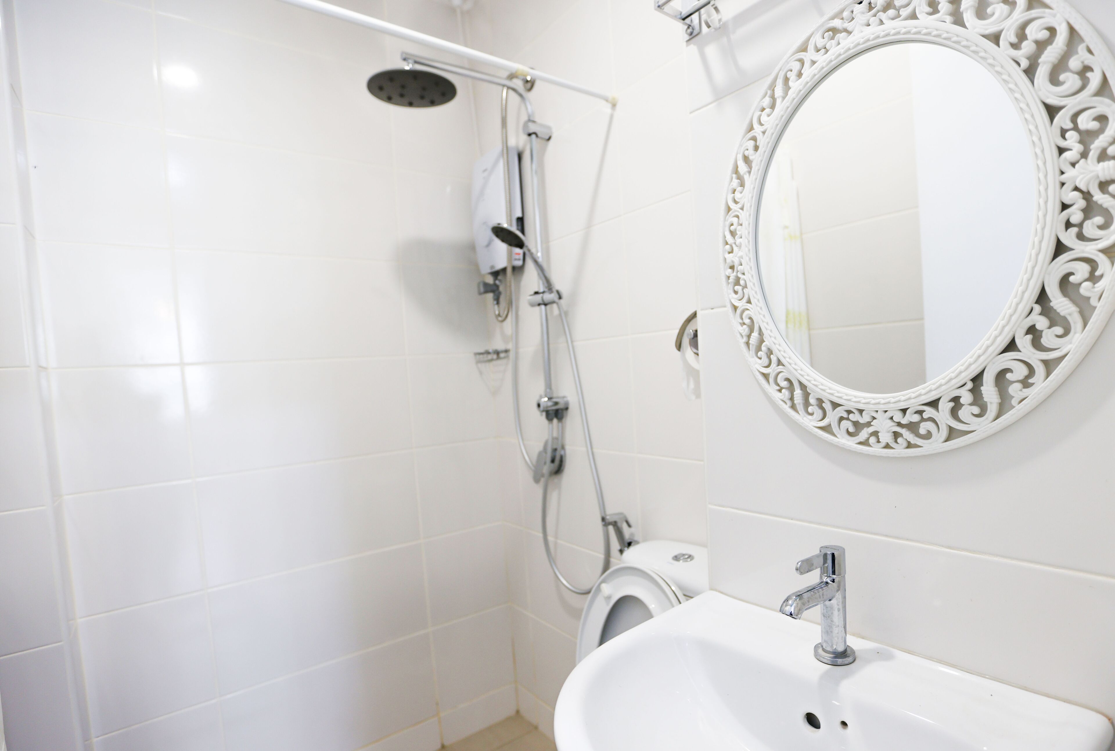 Une salle de bain avec des carreaux blancs, une douche, des toilettes, un lavabo et un miroir décoratif.