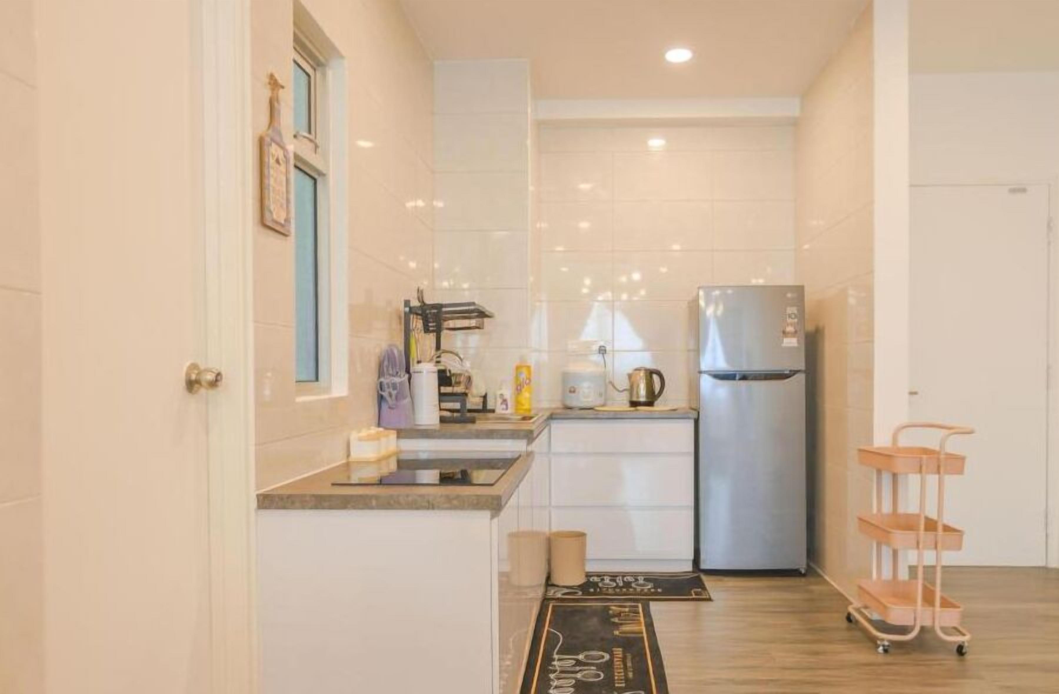 A compact kitchen with a refrigerator, a sink, and a small countertop. There is a window with a view, a door, and a cart with shelves.