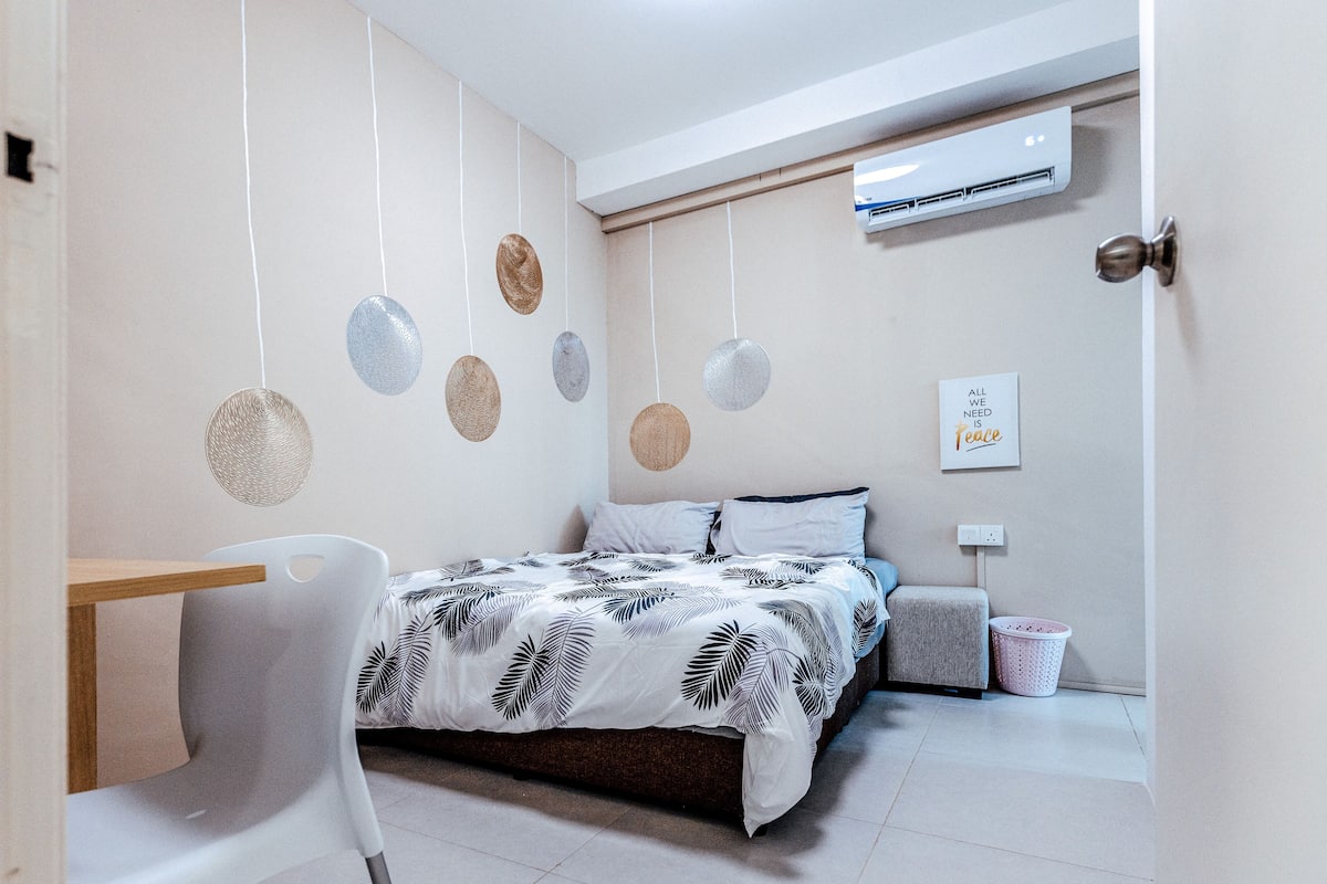 Un dormitorio moderno con una cama, un escritorio y una silla. Hay un aire acondicionado de pared y una cita motivacional en la pared.
