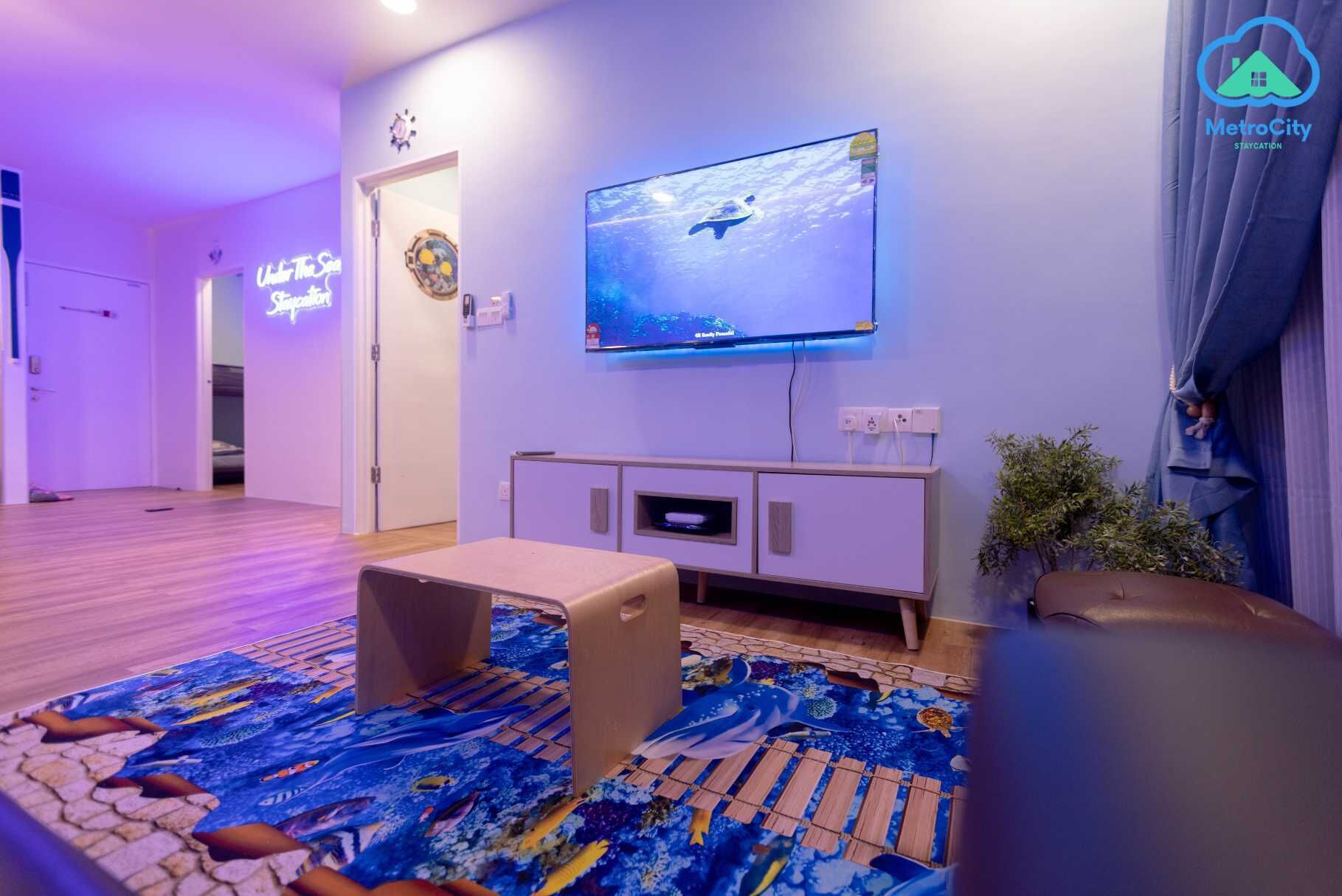 Una sala de estar con un televisor de pantalla plana montado en la pared, piso de madera y una alfombra colorida.