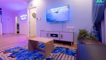 Una sala de estar con un televisor de pantalla plana montado en la pared, piso de madera y una alfombra colorida.