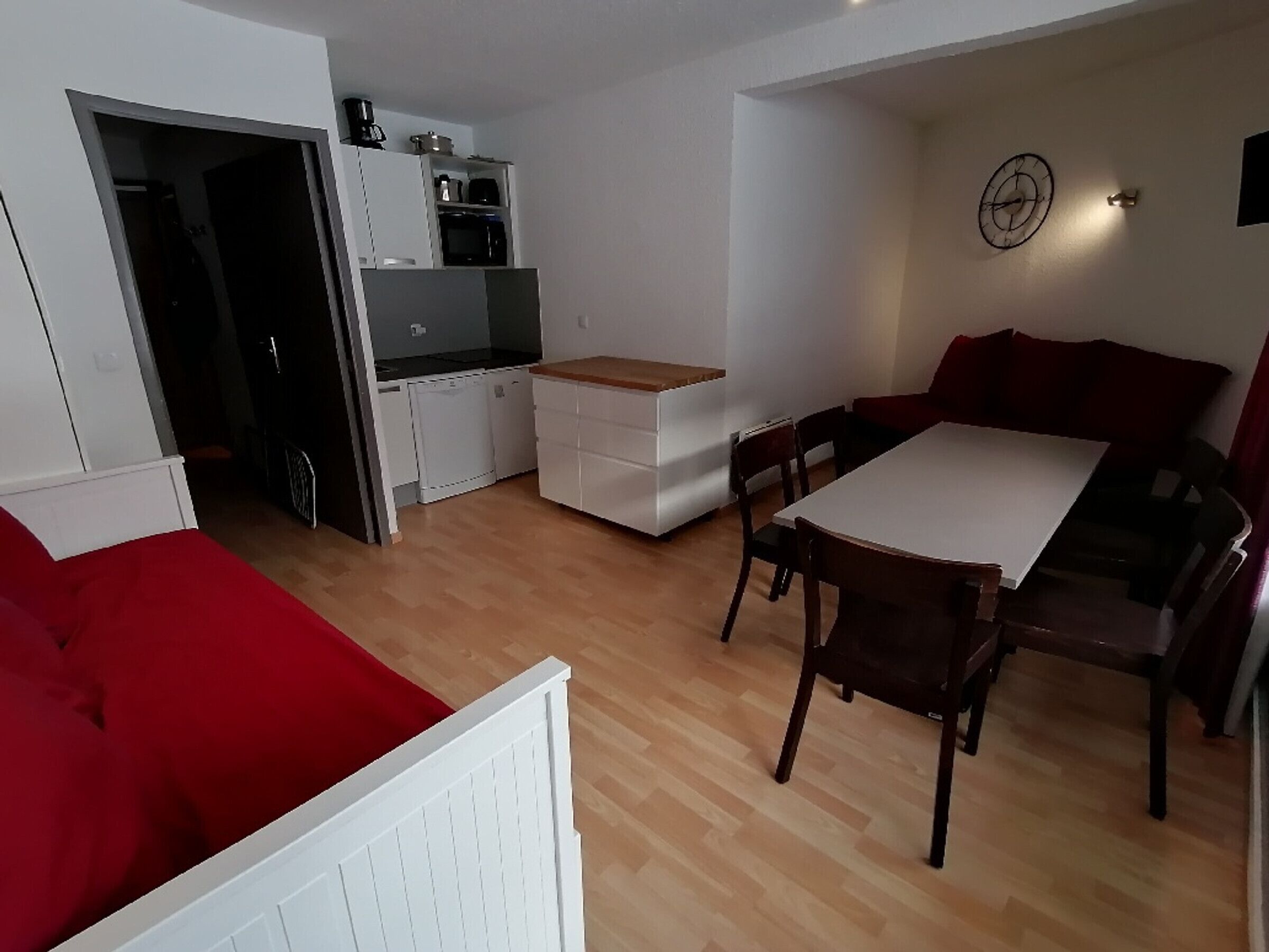 Un espace de vie compact comprenant un coin cuisine, un coin repas avec une table et des chaises, et un canapé rouge.