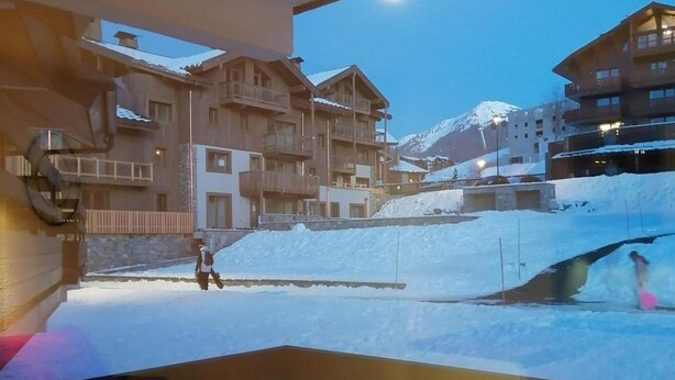 A ski resort with wooden buildings, a snow-covered slope, and a person skiing.