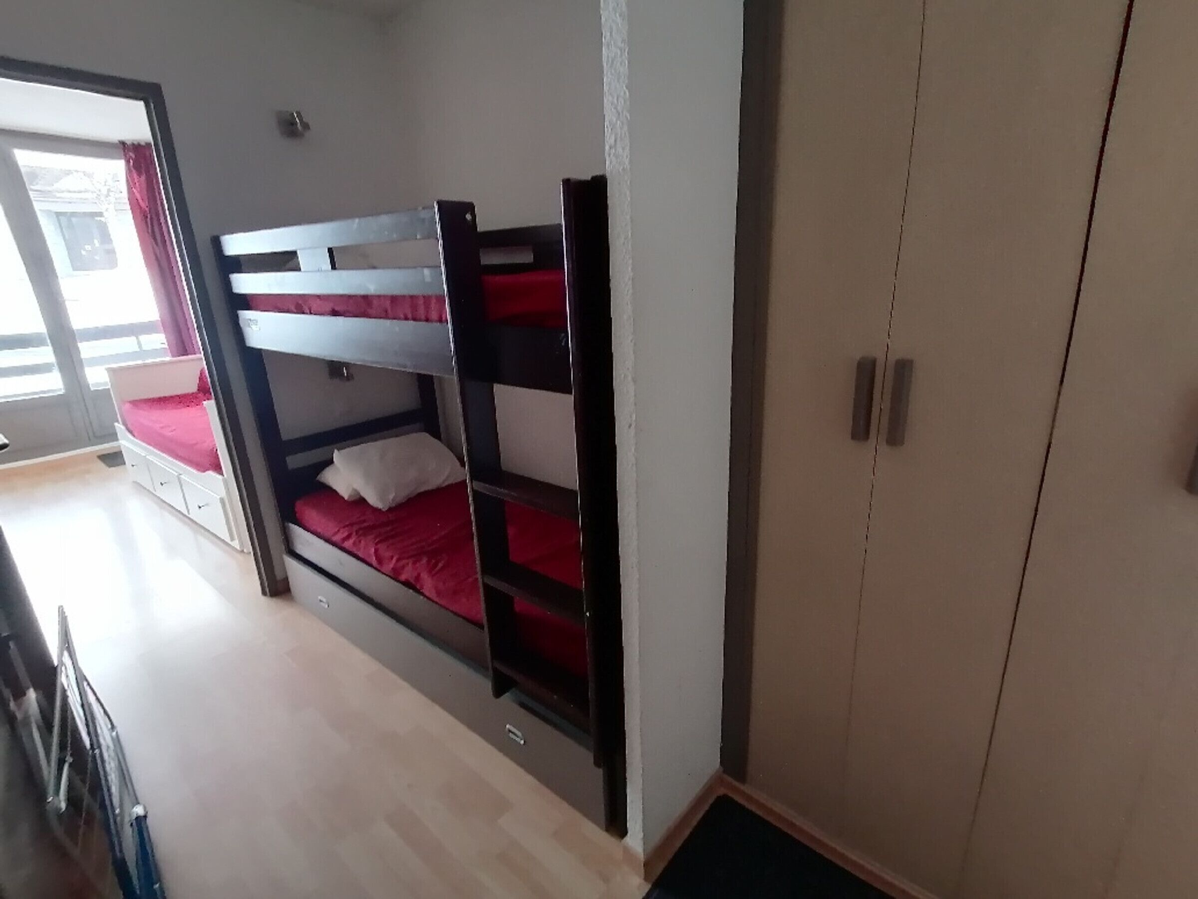 A bunk bed with a red mattress, a white wardrobe, and a door leading to a balcony.