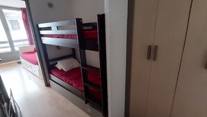 A bunk bed with a red mattress, a white wardrobe, and a door leading to a balcony.