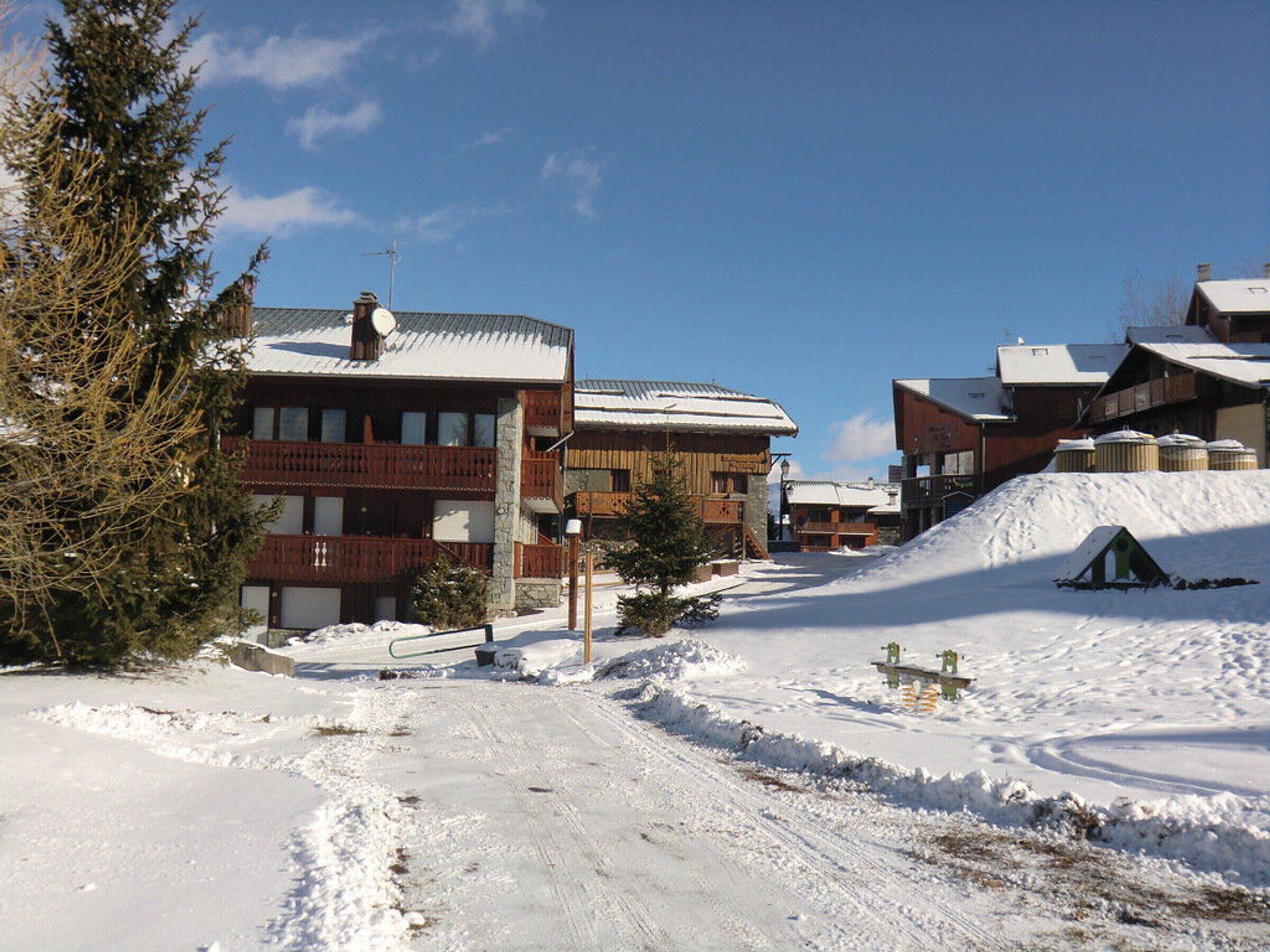 Een met sneeuw bedekte dorp met traditionele houten gebouwen, een heldere lucht en een skilift op de achtergrond.