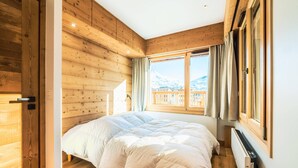 Un dormitorio con una cama grande, paredes de madera, un ventanal con vistas a montañas y un radiador.