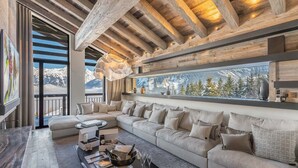 A modern living room with a large sectional sofa, a wooden ceiling, and a large window overlooking a snowy mountain landscape.