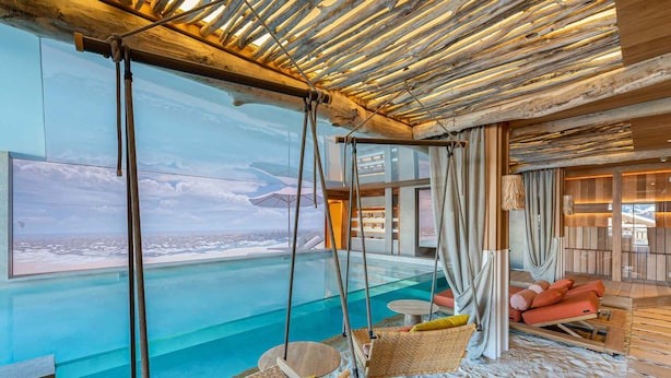 A modern room with a large window overlooking a pool, wooden ceiling, and comfortable seating.