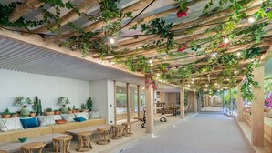 A spacious indoor area with a long bench, wicker chairs, and a ceiling adorned with plants and lights.