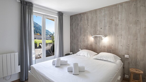 A bedroom with a large bed, a wooden wall, a window with curtains, and a view of a mountain.