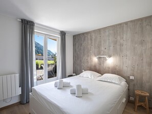 A bedroom with a large bed, a wooden wall, a window with curtains, and a view of a mountain.