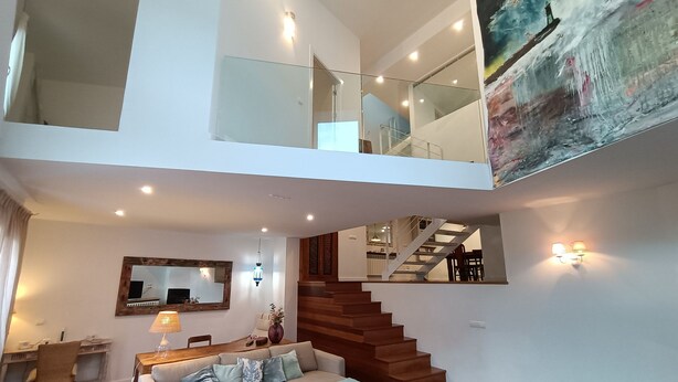 A spacious living area with a staircase leading to an upper floor, a dining area, and a large painting on the wall. - Casa Boutique en Puerto Pesquero de Asturias (Viavélez)
