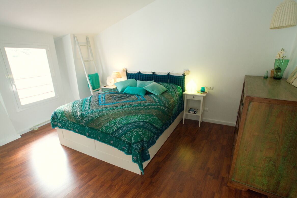 A bedroom with a large bed, a nightstand, a dresser, and a window.