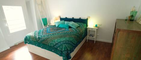 A bedroom with a large bed, a nightstand, a dresser, and a window.