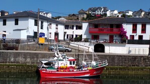 A red fishing boat docked at a harbor with white buildings in the background. - Casa Boutique en Puerto Pesquero de Asturias (Viavélez)