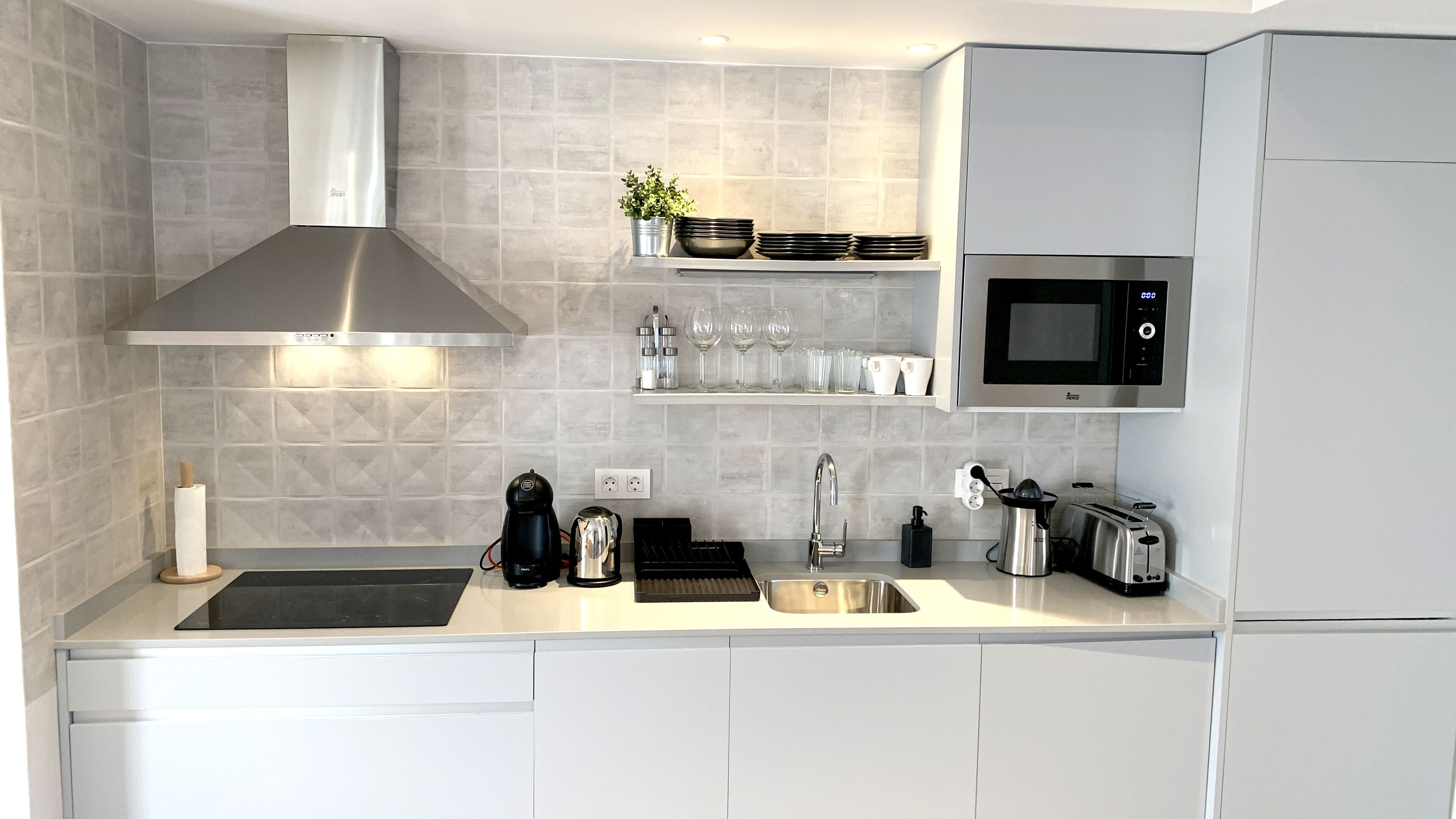 A modern kitchen with a stainless steel range hood, a built-in microwave, and a coffee maker.