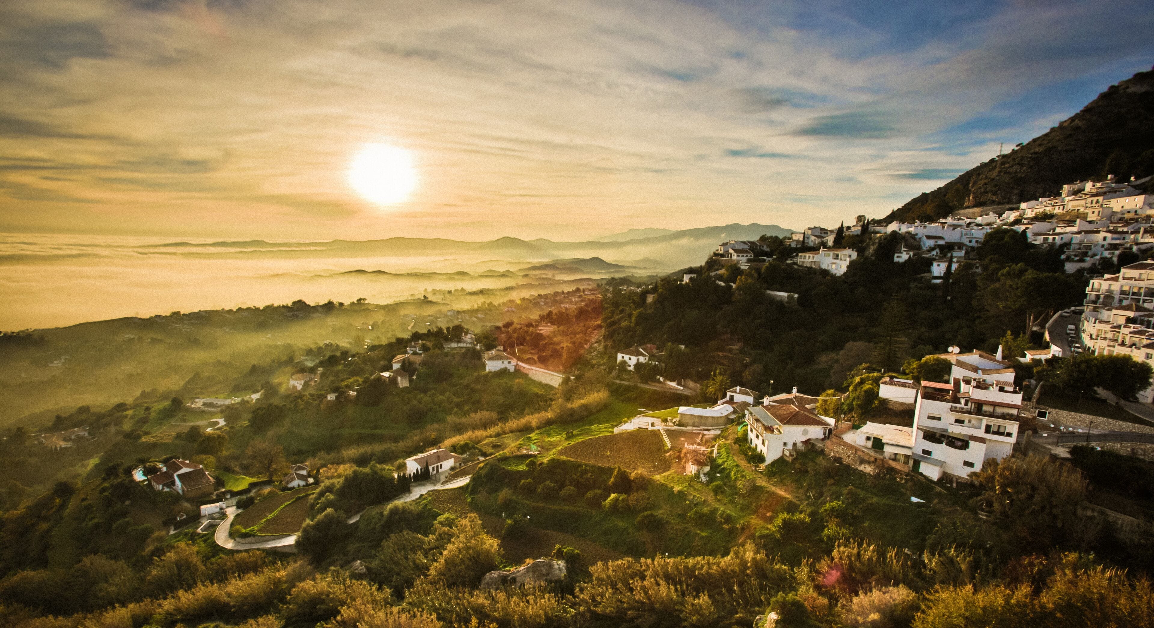 Un pueblo en la ladera con casas blancas tradicionales, campos en terrazas y una vista despejada del paisaje circundante.