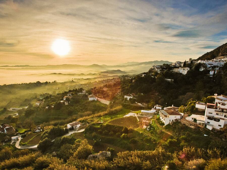 Un pueblo en la ladera con casas blancas tradicionales, campos en terrazas y una vista despejada del paisaje circundante.