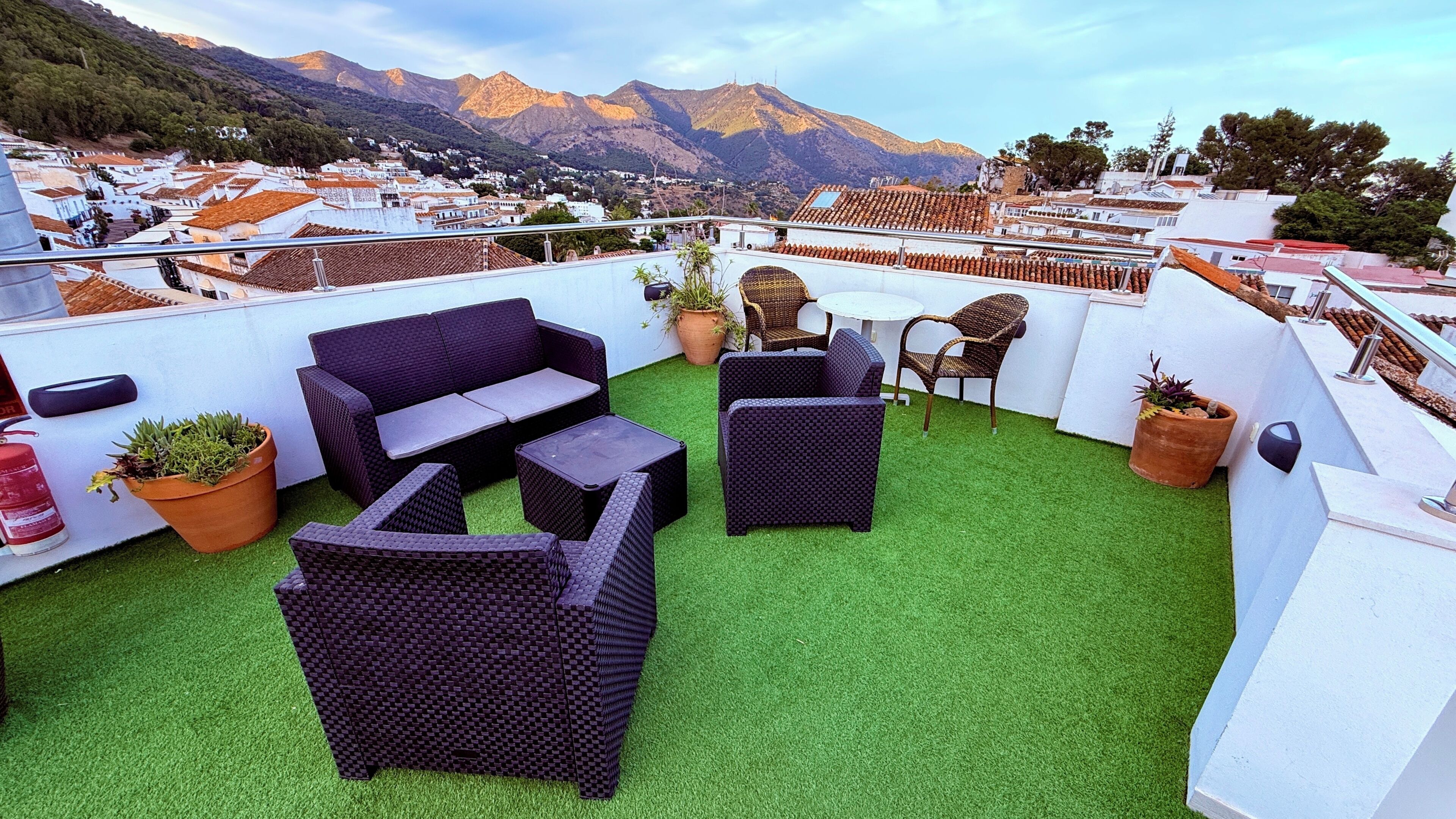 Eine Dachterrasse mit Kunstgrasanlage, Korbmöbeln und Topfpflanzen.