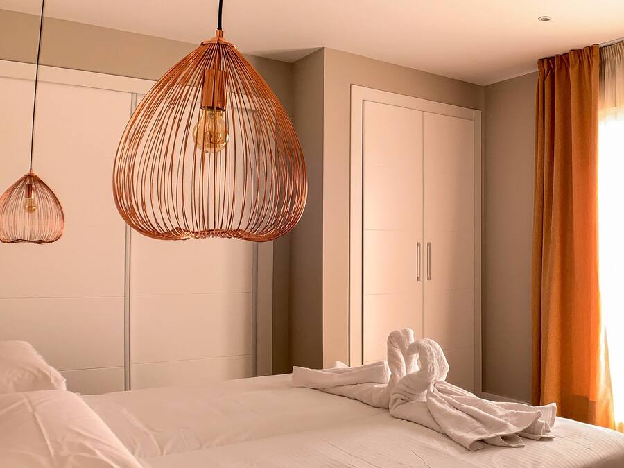Quarto de hotel com cama, duas luminárias pendentes, um guarda-roupa e uma janela com cortinas.