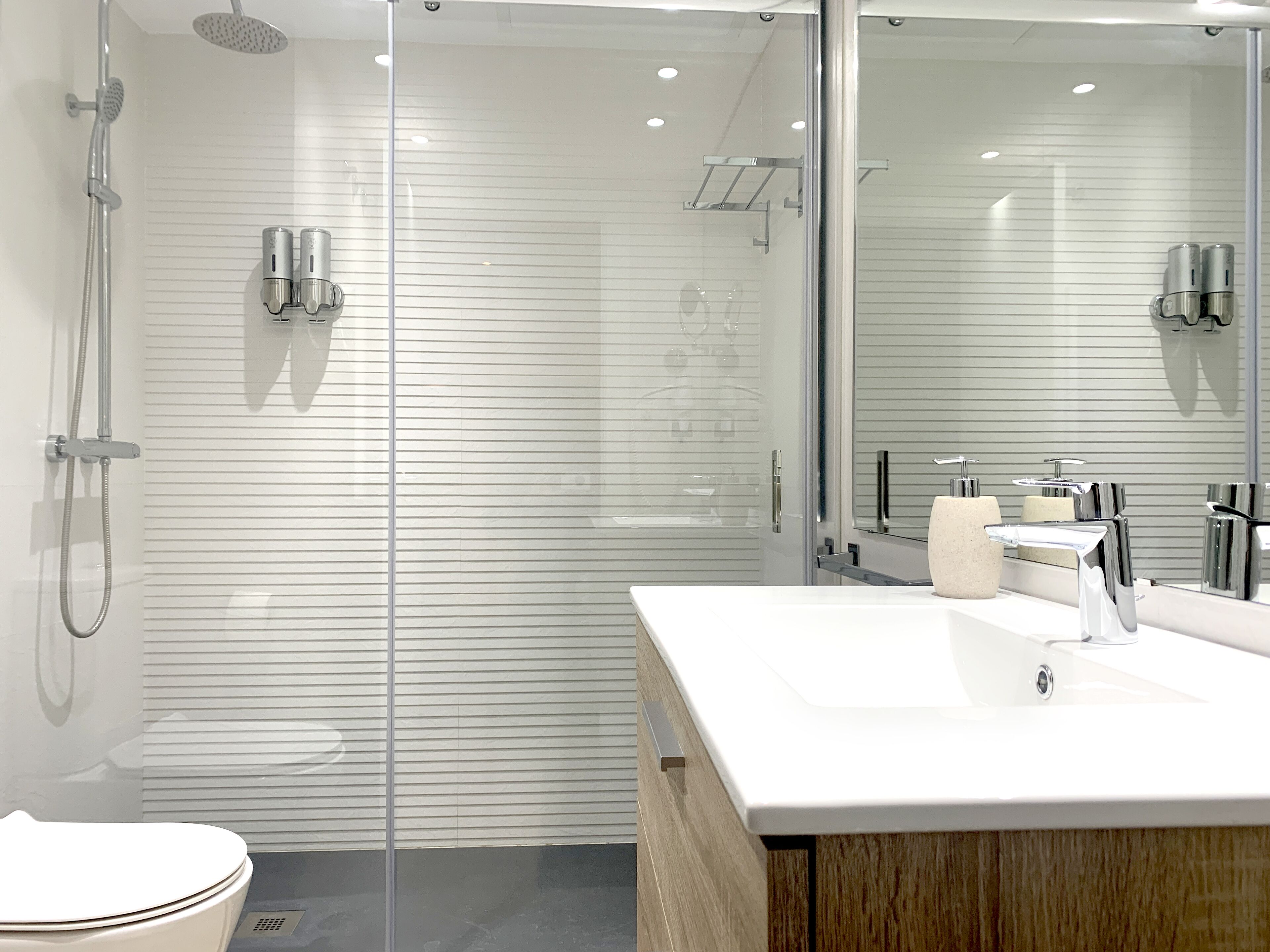 A modern bathroom with a glass shower enclosure, a white sink, and a large mirror.